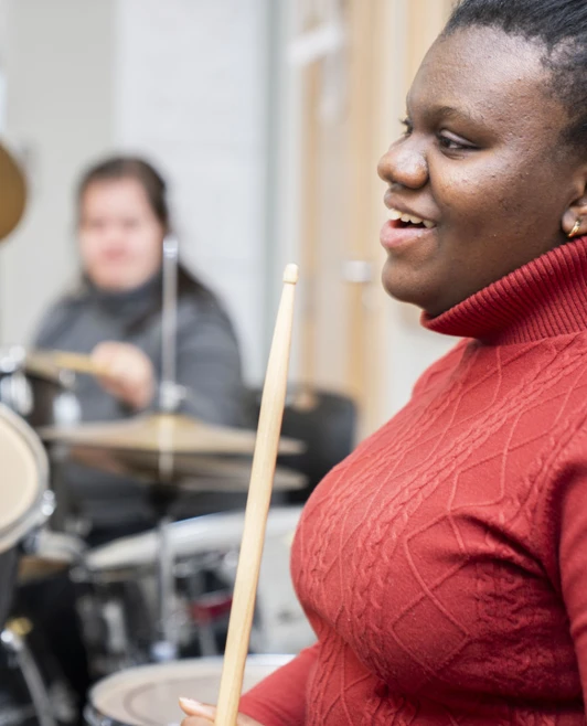 Two young women playing drum kits in a music classroom, smiling and enjoying their drumming session. Two young women playing drum kits in a music classroom, smiling and enjoying their drumming session.